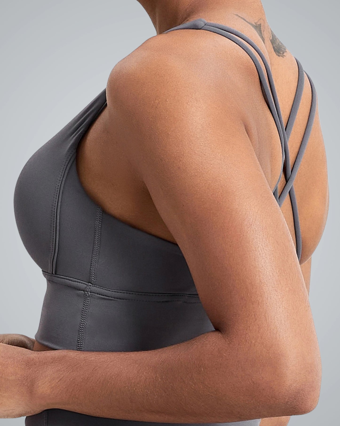 A close-up of a woman wearing a Bandsam gray athletic sports bra, showcasing crisscross straps on the back. Her toned arm and shoulder are visible, emphasizing the design of the activewear.