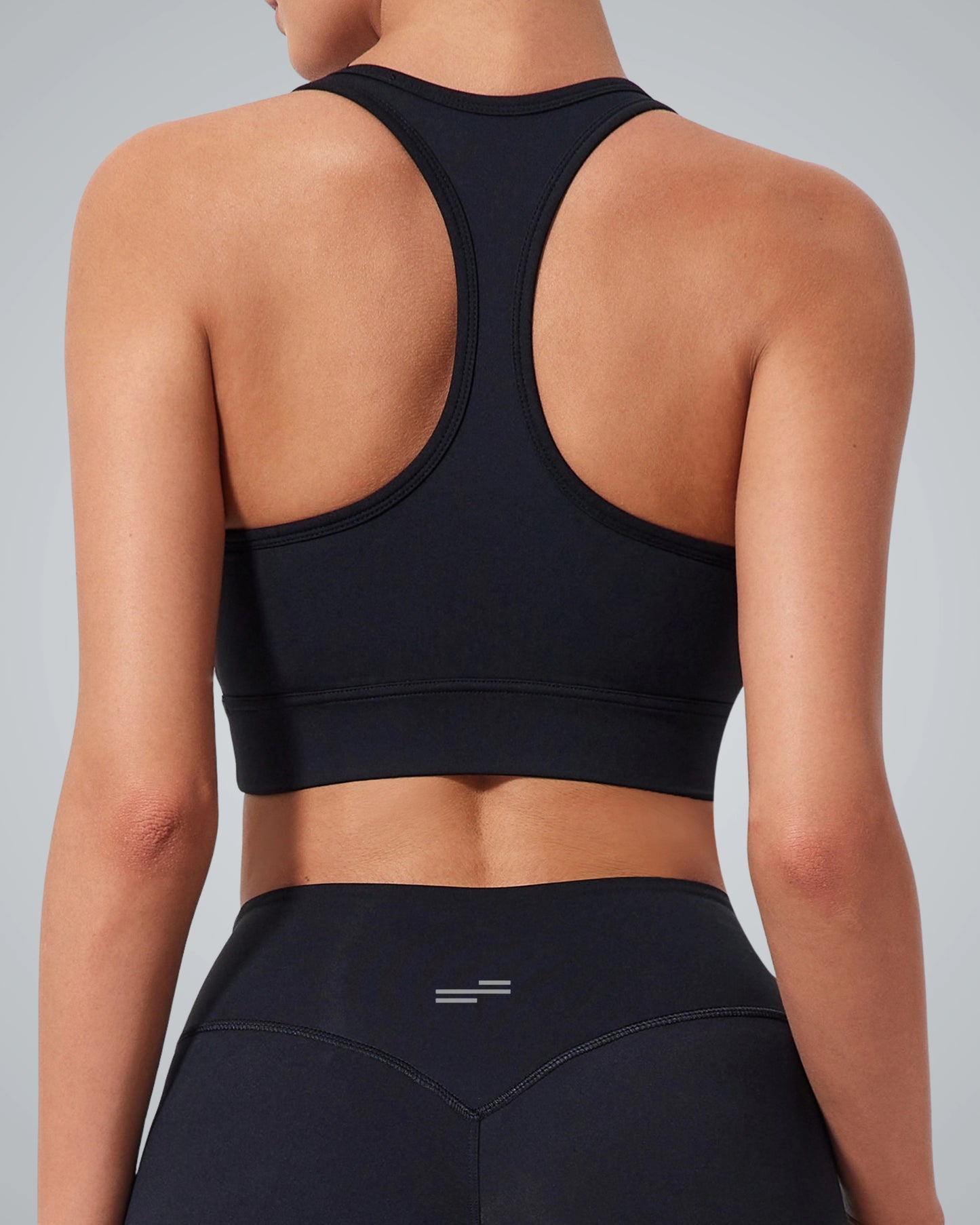 A woman is shown from the back wearing a black high-impact Bandsam sports bra and matching high-waisted Bandsam leggings. The plain gray background draws focus to her supportive athletic outfit from Bandsam, ideal for any active routine.