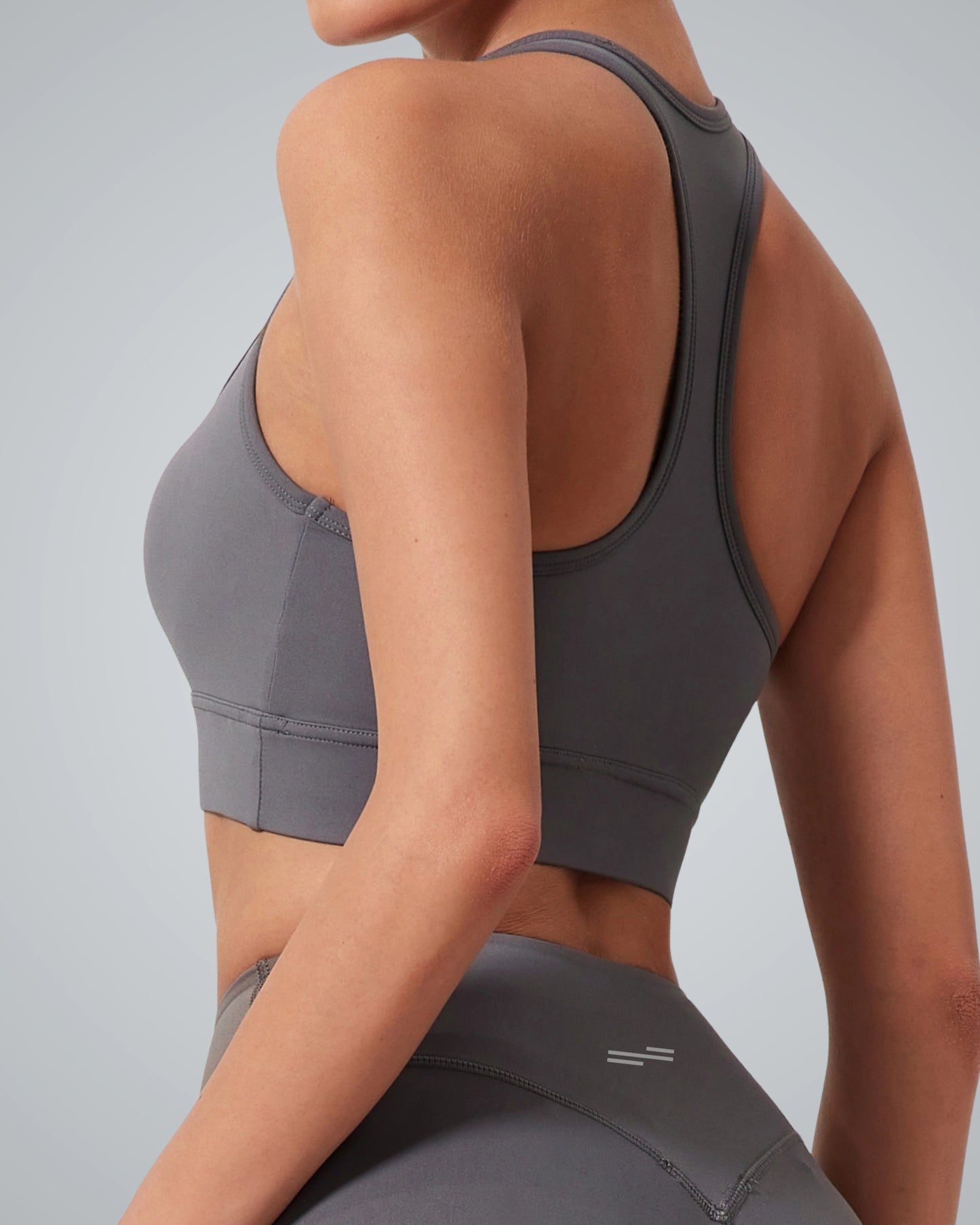 A woman wearing a Bandsam gray high impact sports bra and matching high-waisted leggings, shown from the back against a plain light gray background—perfect support for any active routine.
