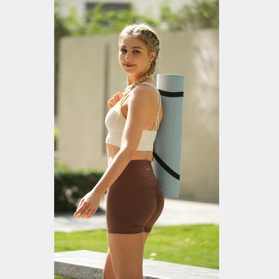 Woman in athletic wear holding a yoga mat outdoors