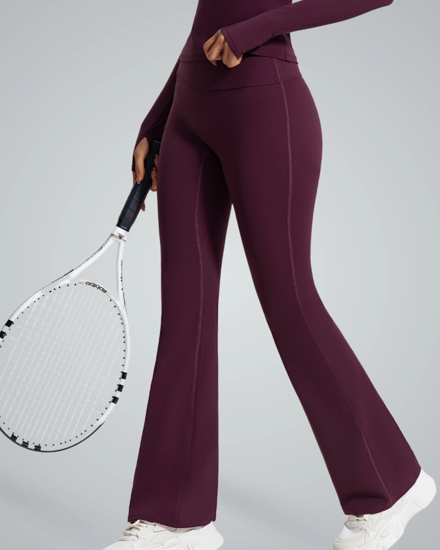 Model wearing Bandsam CurvAlign Pants in maroon, holding a tennis racket. Ideal for stretch, comfort, yoga, and activewear.