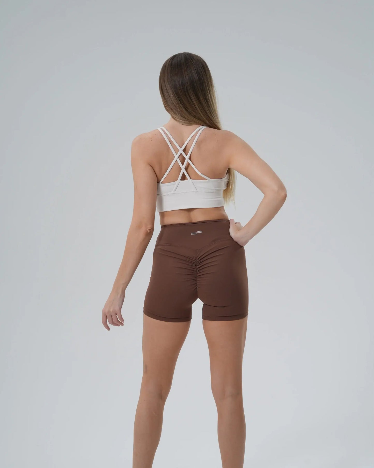 Back view of woman in Bandsam Edge Pro Set, featuring white sports bra and brown shorts, showcasing a minimalist and performance-focused design.