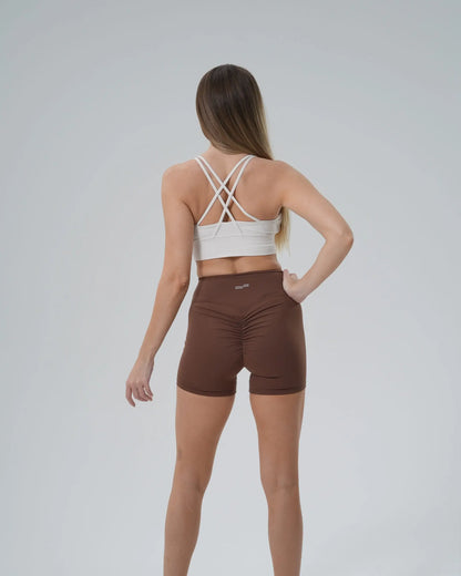 Back view of woman in Bandsam Edge Pro Set, featuring white sports bra and brown shorts, showcasing a minimalist and performance-focused design.