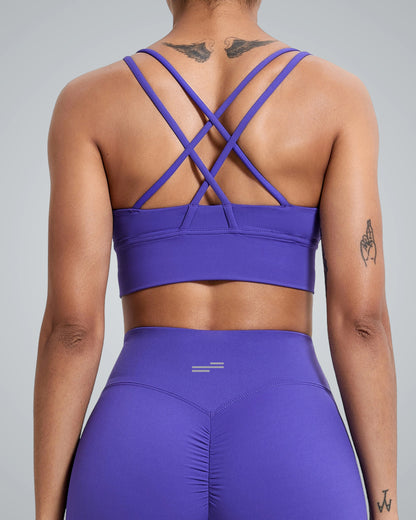 A women wearing a purple breathable Bandsam workout bra with a crisscross design and matching high-waisted leggings, shown from the back. Tattoos are visible on their upper back, arm, and wrist.