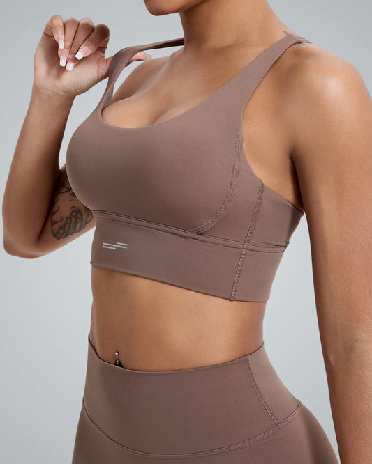 A close-up image of a woman wearing a Bandsam brown sports bra, highlighting its sleek design and fit. The fabric appears smooth and stretchy, perfect for athletic wear. The background is a neutral gray, emphasizing the outfit.