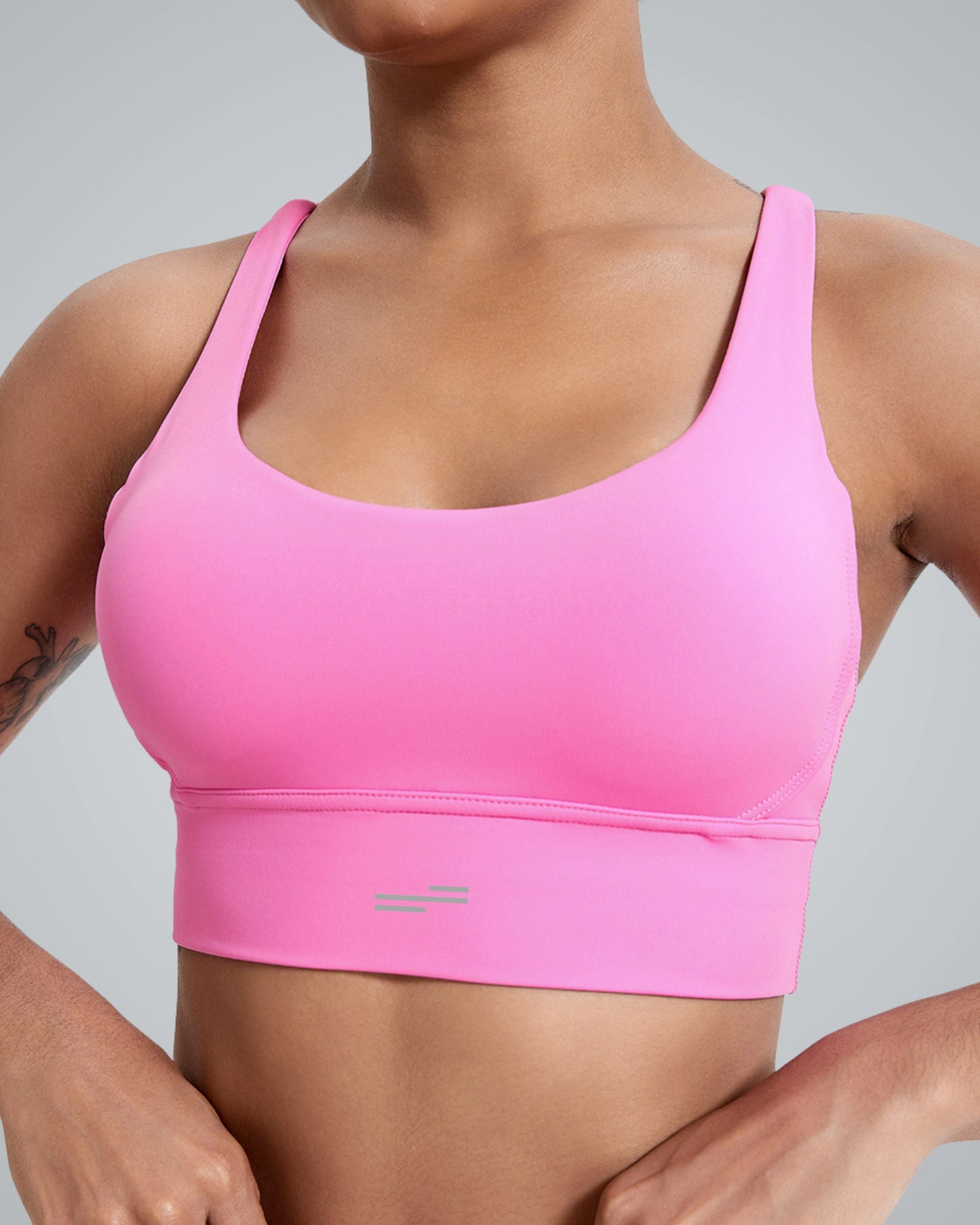 A women wearing a bright Bandsam pink FlexFit Bra with wide straps and a scoop neckline, showing part of their upper body and arms against a plain gray background. This breathable workout bra offers comfy support for any activity.