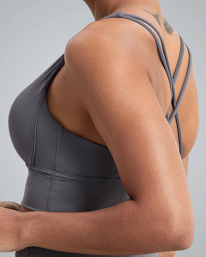 A close-up of a woman wearing a Bandsam gray athletic sports bra, showcasing crisscross straps on the back. Her toned arm and shoulder are visible, emphasizing the design of the activewear.