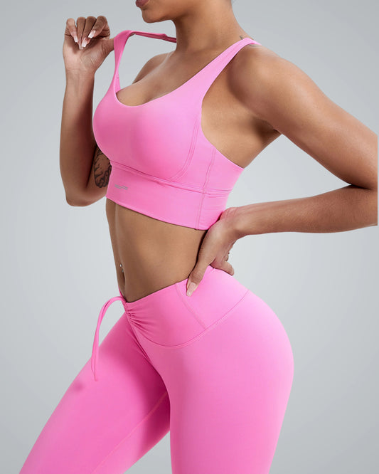 A woman wearing a matching bright Bandsam pink FlexFit Bra and high-waisted leggings poses with one hand on her hip against a plain light gray background.