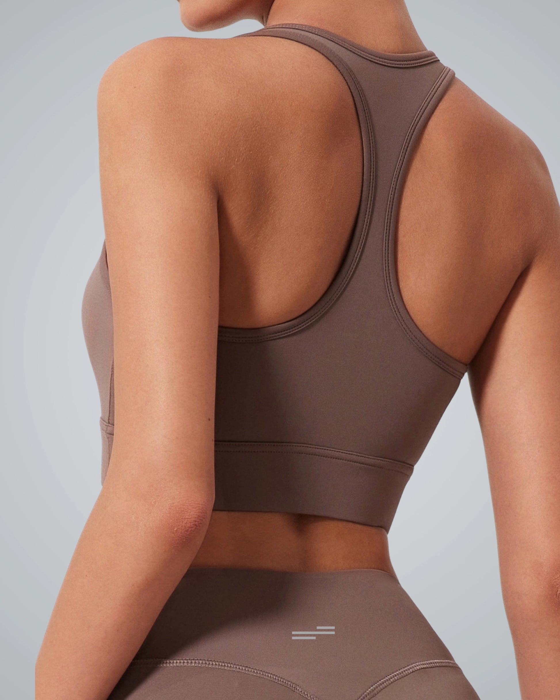 A woman is shown from the back wearing a Bandsam GlowMotion Bra and matching high-waisted leggings. The plain gray background highlights this high impact sports bra, putting the focus on its supportive athletic design.