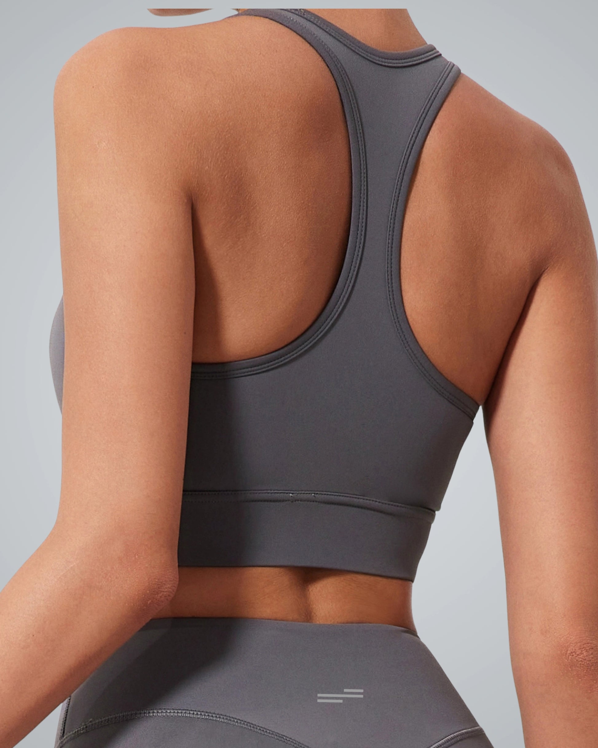 A women wearing a Bandsam fitted gray high impact sports bra and matching leggings is shown from the back against a light gray background. The racerback design offers essential support for any active routine.