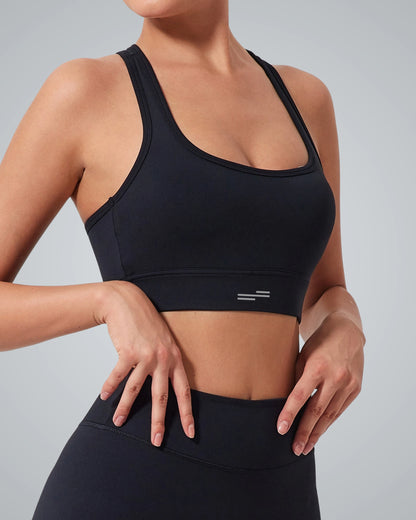 A woman models the Bandsam GlowMotion Bra, a high-impact sports bra paired with high-waisted black leggings, standing against a light gray background. One hand rests on her waist and the other on her hip, with her head out of frame.
