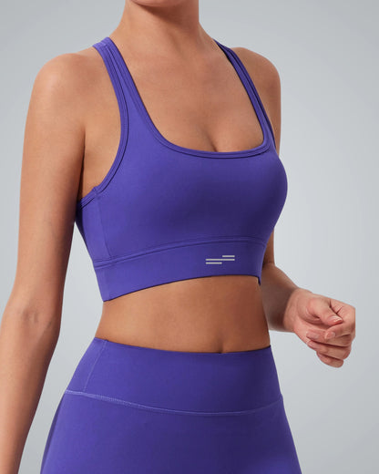 A woman wearing a Bandsam purple high impact sports bra and matching high-waisted leggings stands against a light grey background, showing her upper body and torso.