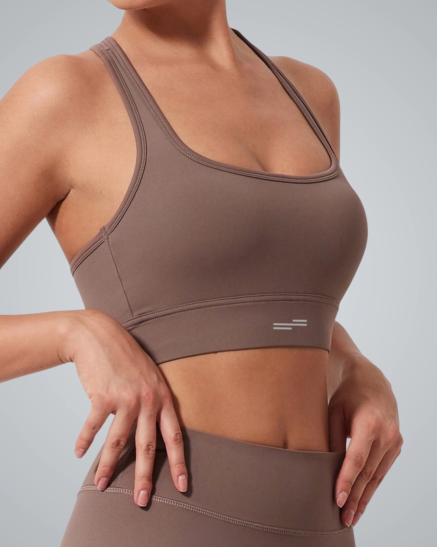 A woman wearing a Bandsam GlowMotion Bra and matching high-waisted leggings poses with her hands resting on her hips, against a plain light gray background.