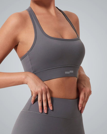 A woman wearing a Bandsam gray high impact sports bra and matching high-waisted leggings stands with her hands resting on her hips, ready to take on any active routine against a plain background.