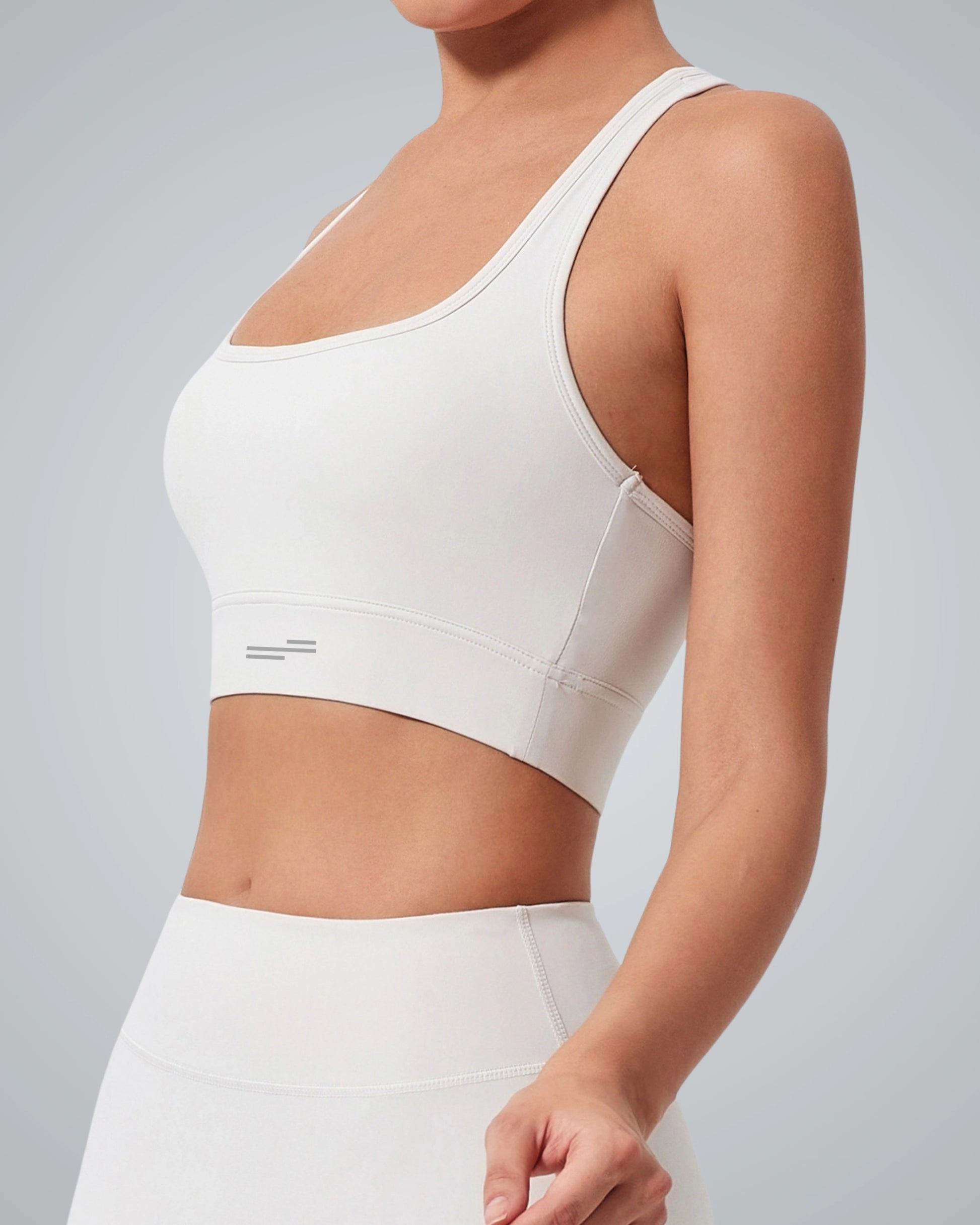 A woman wearing a supportive Bandsam sports bra and matching high-waisted leggings, shown from the side with her head cropped out, standing against a light gray background.