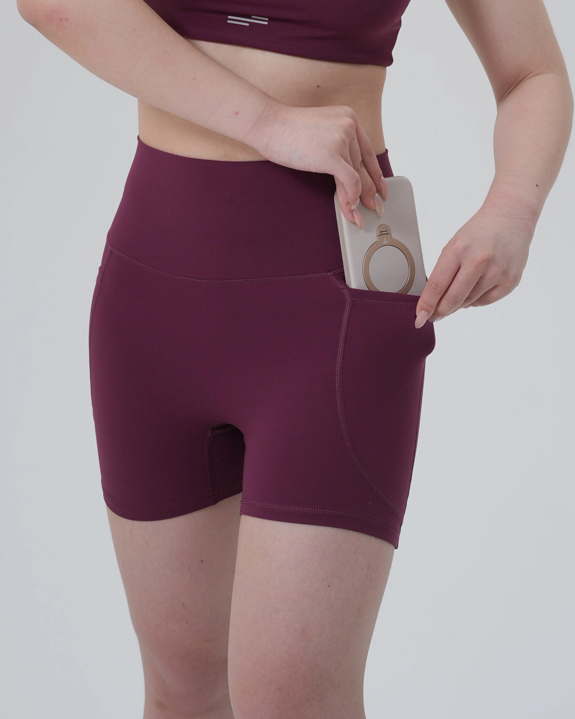 Woman wearing Bandsam's LilaFit high-rise stretch shorts in burgundy, showcasing phone pocket. Perfect for yoga, workout, and activewear.