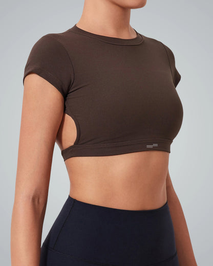 A women wearing a Bandsam fitted ScarletFlow Top with side cutouts and an open back, paired with high-waisted black leggings—perfect for elevating your exercise wardrobe. Shown from the side against a plain light background.