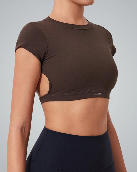 A women wearing a Bandsam fitted ScarletFlow Top with side cutouts and an open back, paired with high-waisted black leggings—perfect for elevating your exercise wardrobe. Shown from the side against a plain light background.