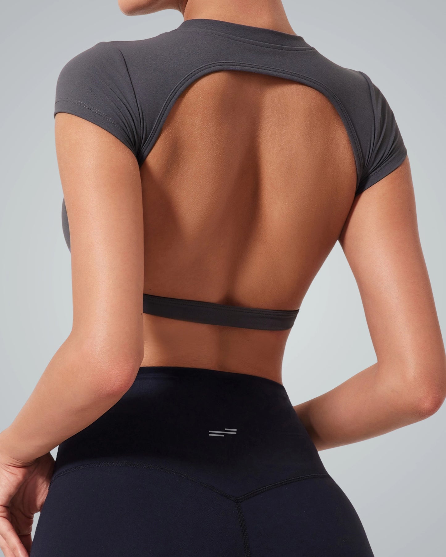 A woman wearing a Bandsam fitted short-sleeve ScarletFlow Top with an open back and high-waisted black leggings, shown from the shoulders to the hips against a plain light background—perfect for updating your exercise wardrobe.
