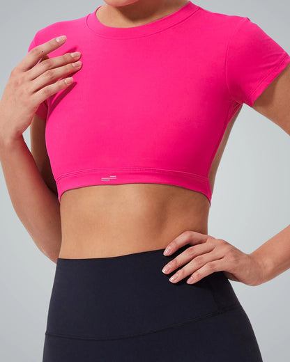 A Women models the Bandsam ScarletFlow Top, a bright pink open back crop top, with high-waisted black leggings—striking a confident pose that elevates any exercise wardrobe against a neutral background.