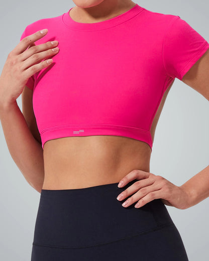 A Women models the Bandsam ScarletFlow Top, a bright pink open back crop top, with high-waisted black leggings—striking a confident pose that elevates any exercise wardrobe against a neutral background.