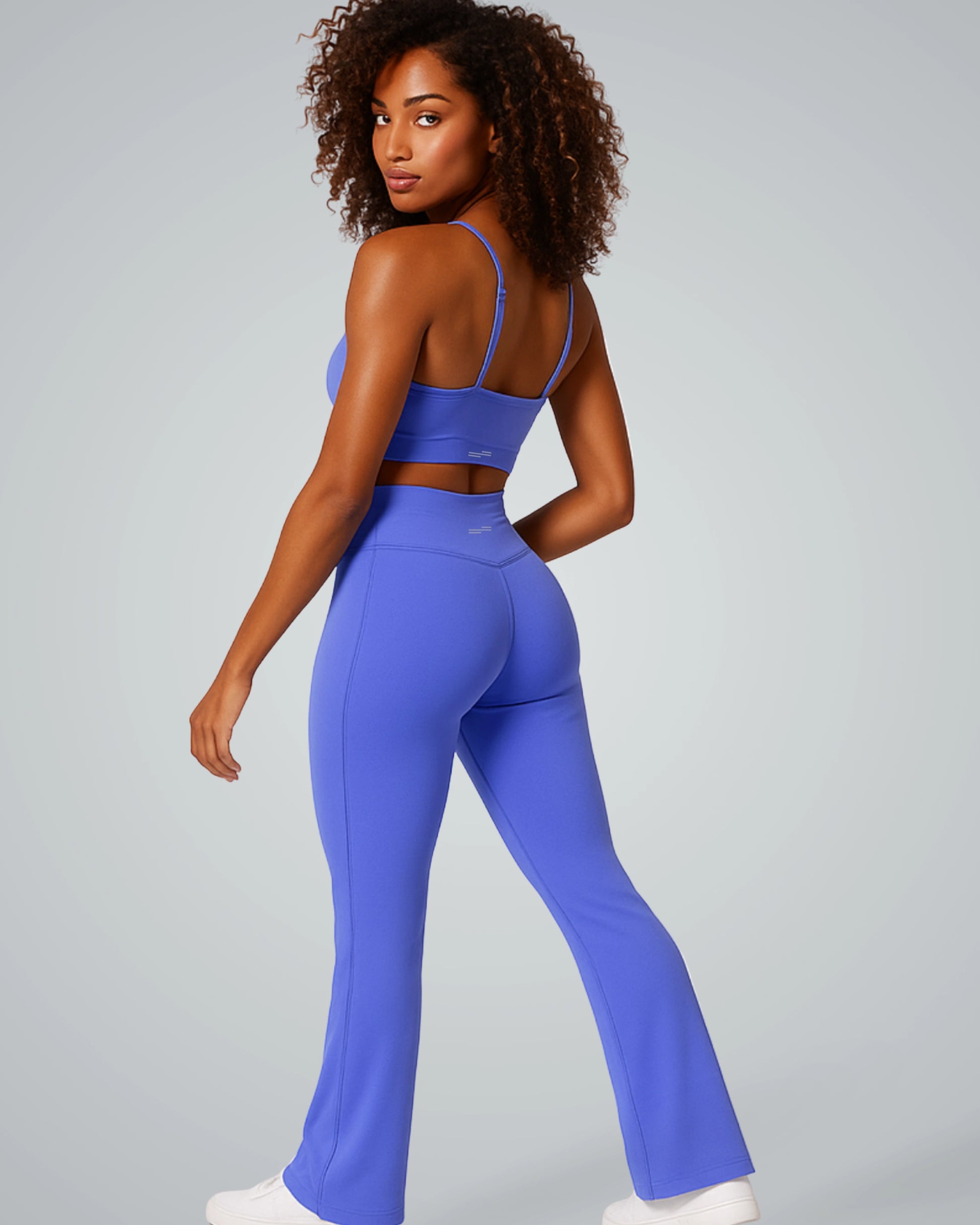 Woman modeling Bandsam SculptEase stylish activewear set with twist-front sports bra and high-waisted V-shaped flared trousers in blue.