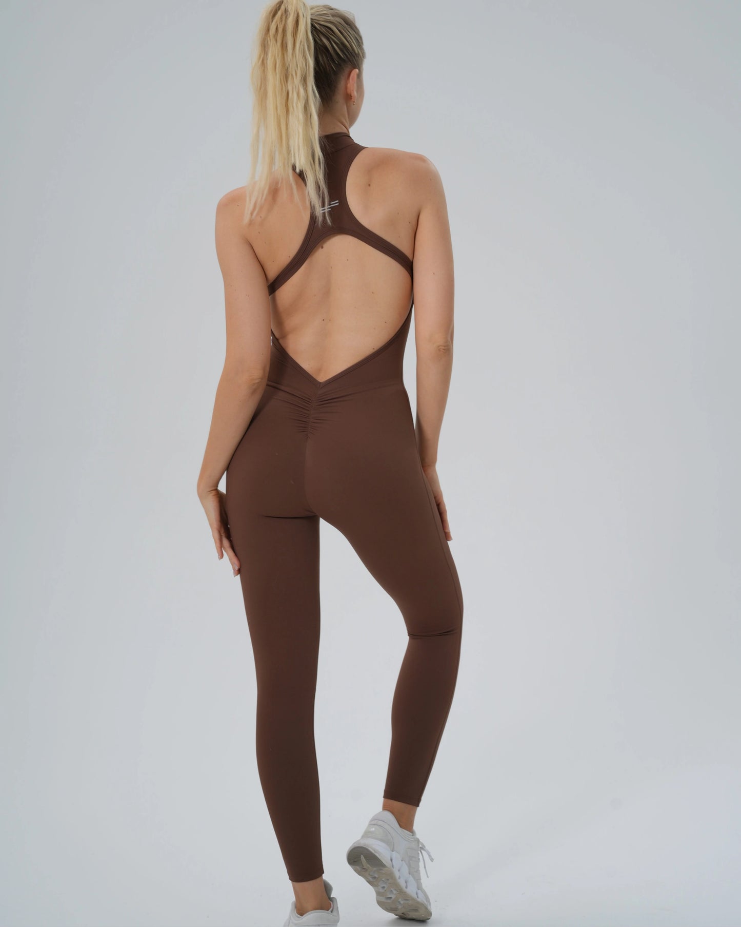 Back view of woman wearing Bandsam VelocityVibe Jumpsuit, showcasing flexible, soft brown activewear ideal for yoga and lounging.